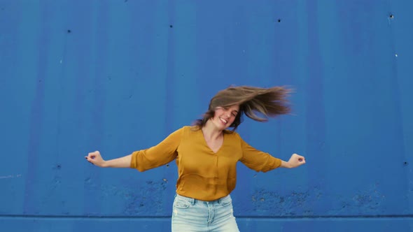 Young dancing woman in front of a blue wall