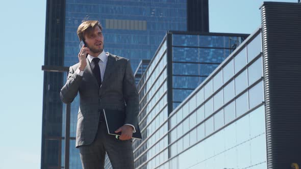 Businessman, Top Manager in a Suit Stands Near a Glass Skyscraper and Talking on a Mobile Phone