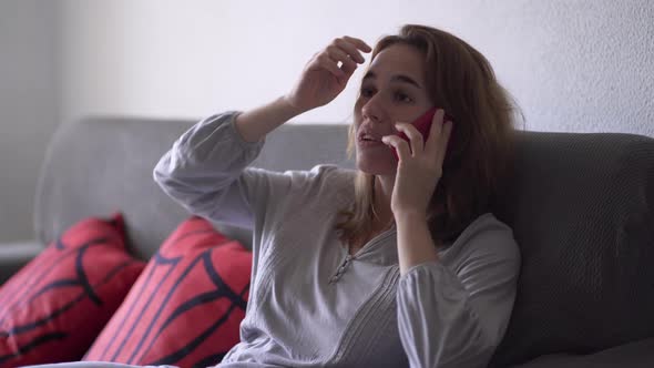 Young Woman Sitting on Sofa in Pajamas Talking on Mobile Phone