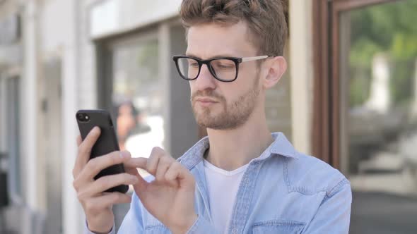 Casual Young Man Cheering Success on Smartphone Sitting in Outdoor Cafe