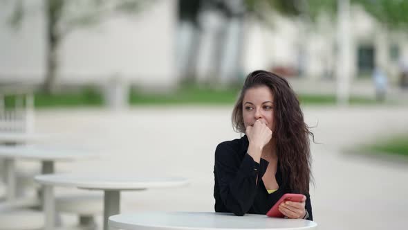 Thoughtful Woman is Sitting on Open Terrace of Cafe in Summer Day Resting in Park