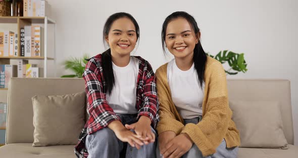 Twin girls waving hand while sitting on couch