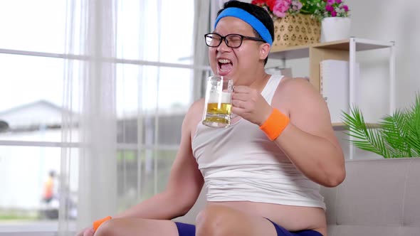 Funny fat Asian guy in sportswear doing exercise weight training by dumbbell and drinking beer