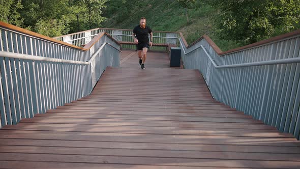 Active Man Runs on Wooden Stairs Leading to Footbridge