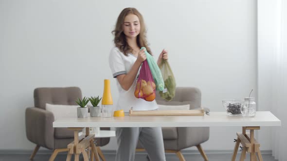 Young Smiling Woman Putting Bags with Fruit and Vegetables on the Table in Modern Office
