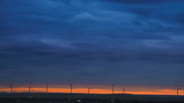 Motion the Blades of a Large Wind Turbine in a Field Against a Background of Orange Sunset on the