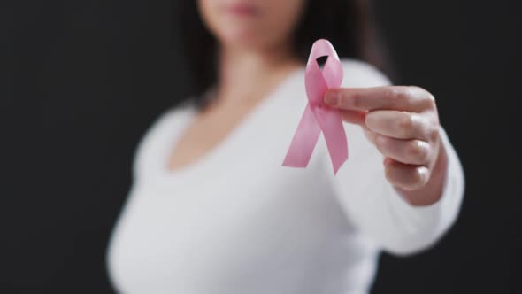 Mid section of woman holding a pink ribbon against black background