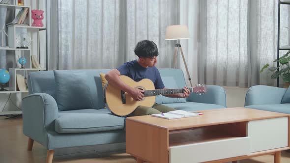 Asian Boy Composer With Note Book And Playing Guitar At Home