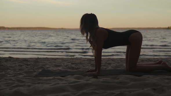 Young Fit Woman Practices Yoga Wearing Black Body a Sandy Beach Using a Mat