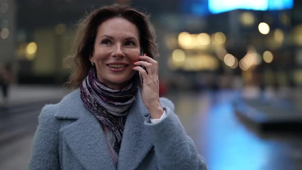 Portrait of a Woman in a Light Coat and Scarf and with Bright Nails at Dusk Against the Background