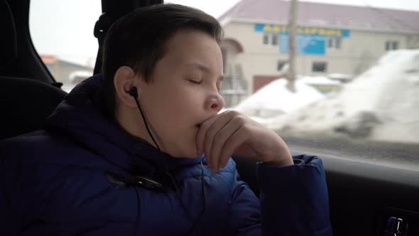 Teen Boy Ride in the Back Seat of the Car and Listen Music in the Headphones