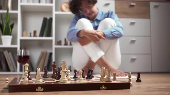 Young Woman Playing Chess On The Floor At Home. A European Girl Plays Chess With A Glass Of Wine