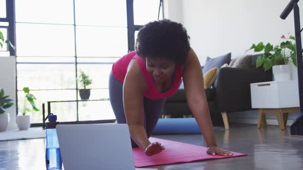 African american female plus size with laptop kneeling on exercise mat working out