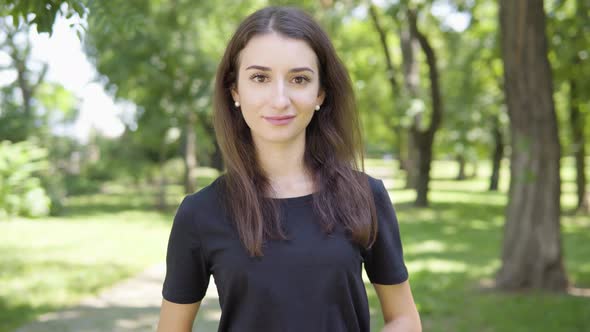 A Young Turkish Woman Smiles at the Camera in a Park on a Sunny Day