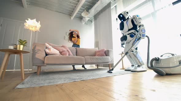 Young Woman Is Talking on the Phone While the Droid Is Hoovering. Robot, Human-like Cyborg Concept