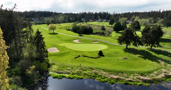 Aerial of putting green surrounded by sand traps and a water feature.