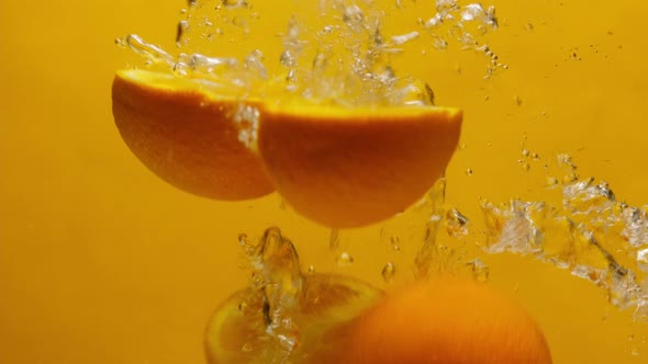 Closeup of Falling Sliced Oranges Into the Water on Orange Background Making a Cocktail of Citrus