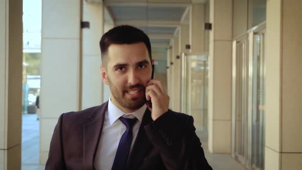 Close Up View of Businessman Dressed in Shirt Talking Smartphone While Walks on the Background of a