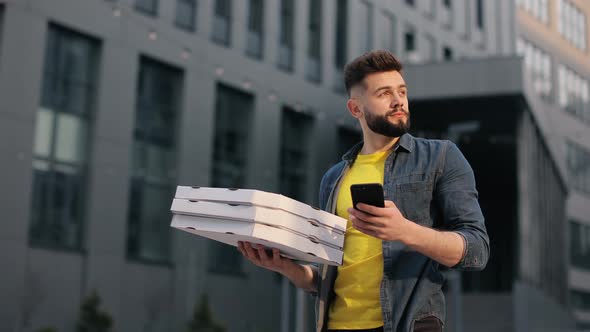 The Food Delivery Guy is Standing and Texting on a Smartphone