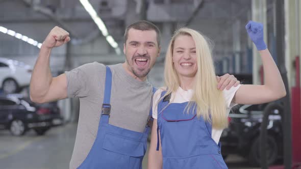 Young Caucasian Man and Woman Showing Strength Gesture, Looking at Camera and Smiling. Professional