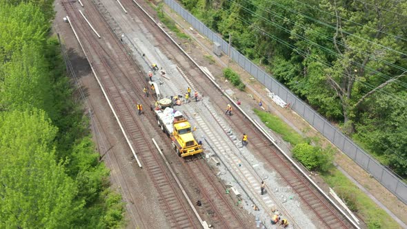 an aerial view over workers repairing train tracks on a sunny morning. The drone camera tilted down
