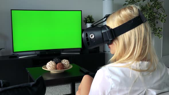 Young Blond Woman Uses Virtual Reality Glasses in Home, in Living Room - Green Screen Television