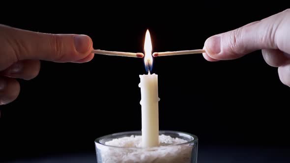 Hands Lights a Two Matches on a Flame Burning Candle on a Black Background