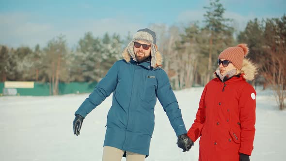 Woman And Man Holding Hands Walking In Parka. Relax Lifestyle Having Fun In Cold Day. Snowy Park.