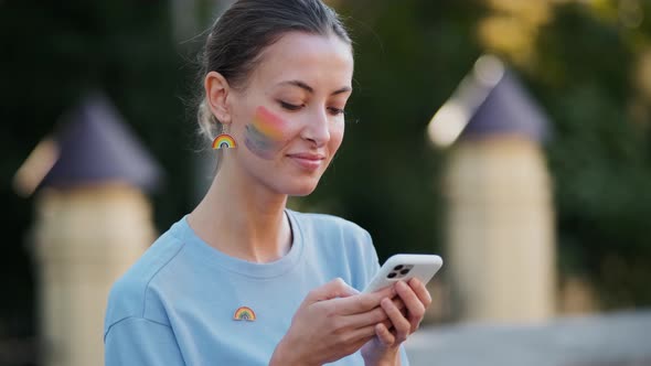 A smiling woman with rainbow make-up typing message using her phone during pride gay