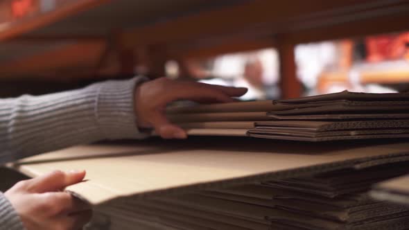 A Girl In A Hardware Store Chooses Cardboard Boxes. The Girl's Hand Pulls A Cardboard Box