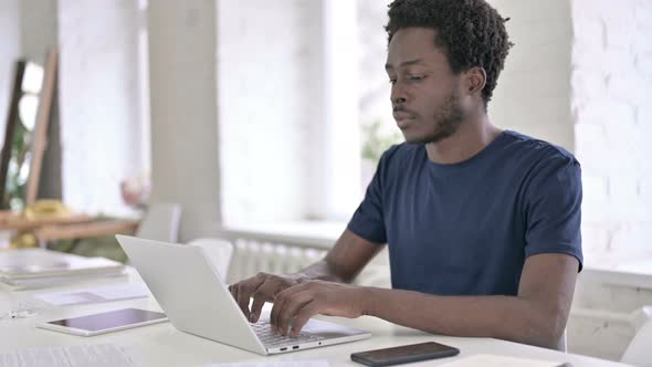 Young African Designer Thinking and Working on Laptop