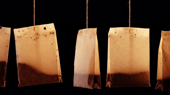 Set of Used Tea Bags Hang Swaying on Thin Threads on Black