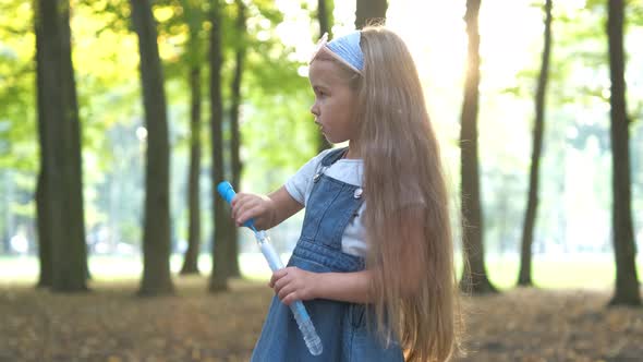 Little Happy Child Girl Blowing Soap Bubbles Outdoors in Summer Park