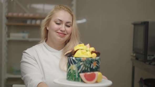 Young adult woman chef decorating cake with mango, passion fruit, grapefruit and blueberry.