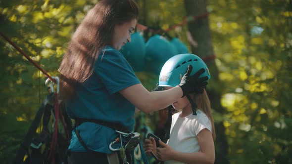 Woman Instructor Putting on a Little Girl Protective Helmet for the Rope Adventure