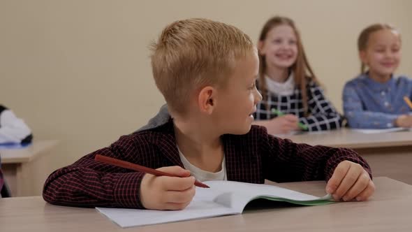 A Portrait of a Little Boy at School at a Desk He Raises His Hand to Answer