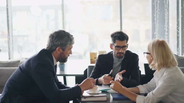 Bearded Men Discussing Contract Details with Senior Businesswoman in Cafe