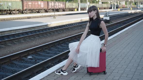 Pretty Girl in Blackwhite Dress Sitting on Suitcase in Fixed Pose at Railway
