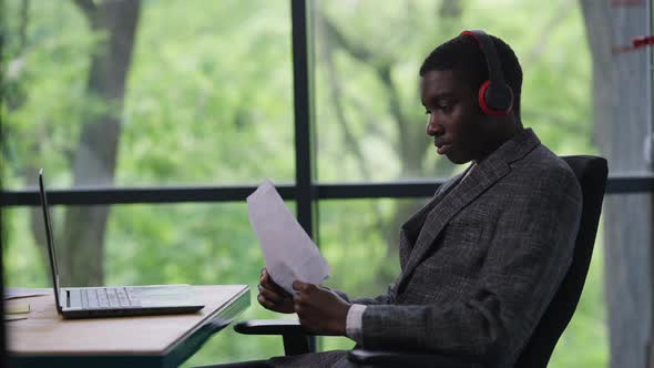 Young Handsome African American Man in Headphones Listening to Music Analyzing Documents in Office