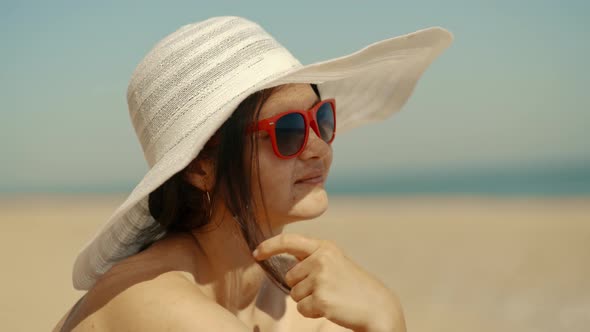 A Young Girl in a White Hat Sits on the Seashore and Looks Into the Distance