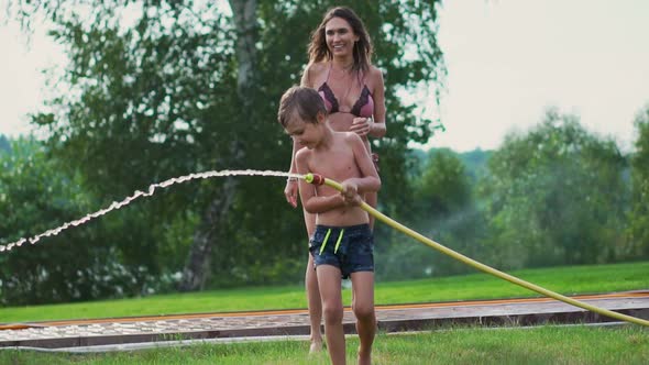 Mom and Son Playing on the Lawn Pouring Water Laughing and Having Fun on the Playground with a Lawn