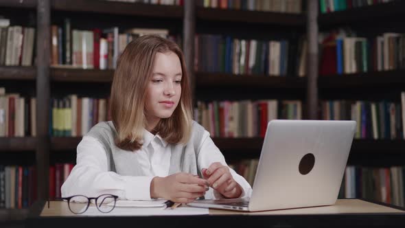 Teen Girl Sitting in Library Answering Teacher While Having Online Lesson Distance Learning