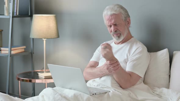 Old Man with Laptop Having Wrist Pain in Bed 