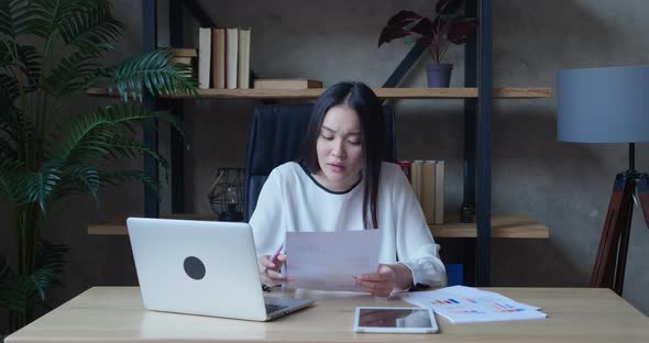 Focused Asian Millennial Woman Studying From Home Online Training Listening to Teacher Taking Notes