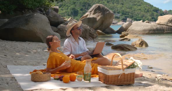 Couple of Young People Resting on the Secluded Beach Having Picnic Rest and Work at the Same Time