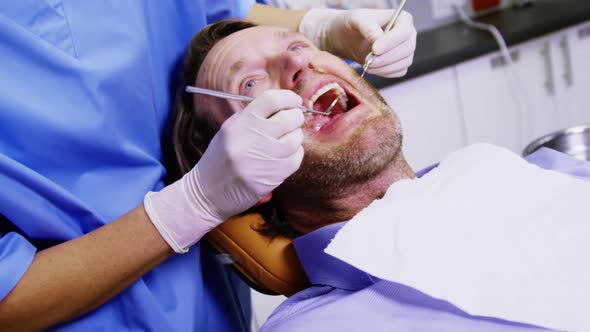 Dentist examining a male patient with dental tools