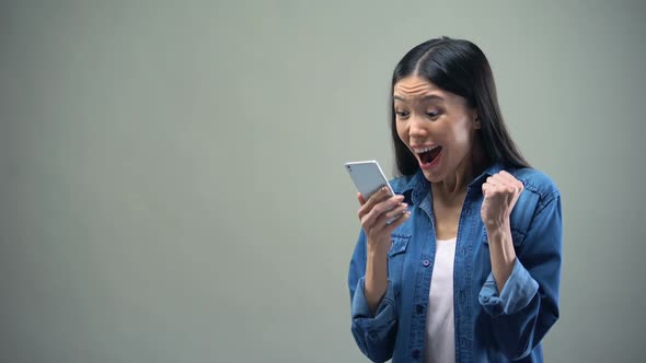 Asian Lady Sincerely Rejoicing Holding Smartphone, Favorable Tariffs for Calls