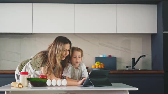 Pretty Mom Stands in Kitchen Leaning Over Her Daughter