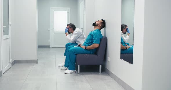 Stressed Male Doctors Sitting on Couch in Clinic Corridor