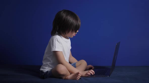 Boy Child in a White Tshirt and Shorts is Sitting on a Bed Against a Blue Wall of the House